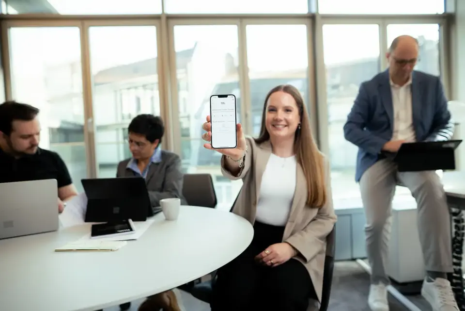 Kolleginnen und Kollegen von Intertours arbeiten gemeinsam an Laptops und Tablets; eine Kollegin zeigt ein Smartphone.